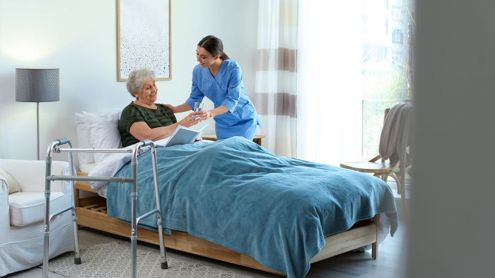 A Nurse Holding Hands With An Elderly Patient In Bed, They Are Both Smiling At Each Other